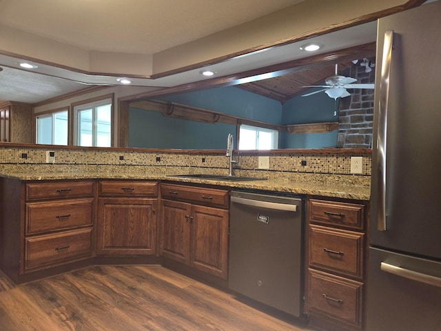kitchen featuring light stone counters, a sink, stainless steel appliances, backsplash, and vaulted ceiling