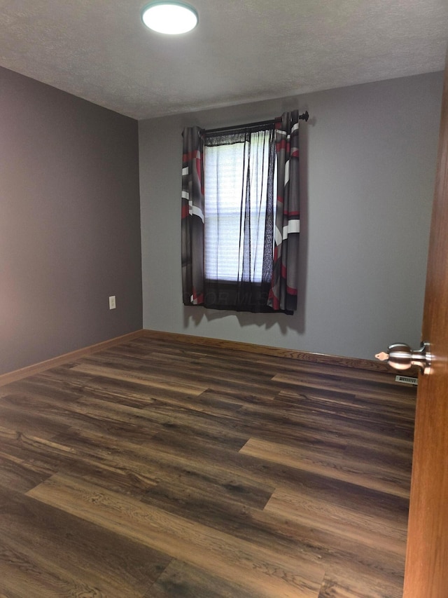 unfurnished room with baseboards, a textured ceiling, and wood finished floors