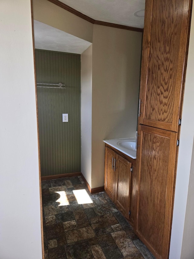 bathroom featuring crown molding, baseboards, vanity, and stone finish flooring