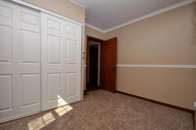unfurnished bedroom with a textured ceiling, baseboards, a closet, ornamental molding, and carpet
