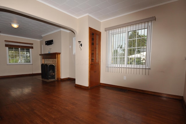 unfurnished living room with arched walkways, a brick fireplace, wood finished floors, baseboards, and ornamental molding