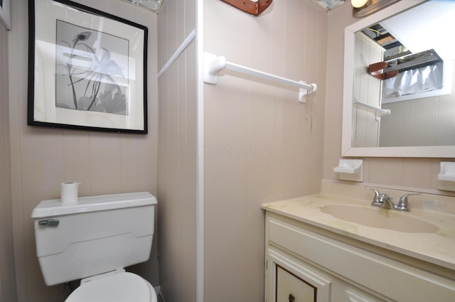 half bath with vanity, a decorative wall, and toilet