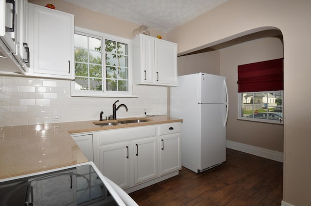 kitchen featuring freestanding refrigerator, dark wood-style floors, white cabinets, tasteful backsplash, and a sink