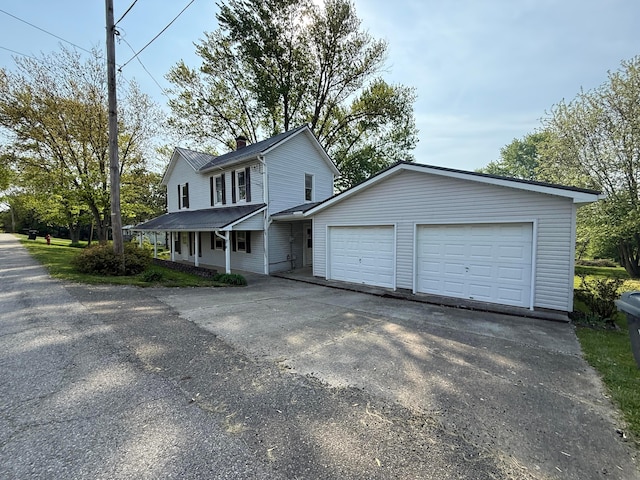 view of front facade featuring a porch, driveway, a chimney, and a garage
