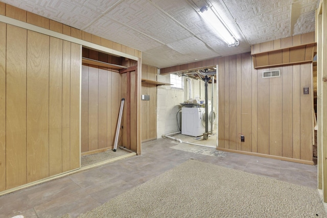 basement with visible vents, baseboards, an ornate ceiling, wooden walls, and separate washer and dryer