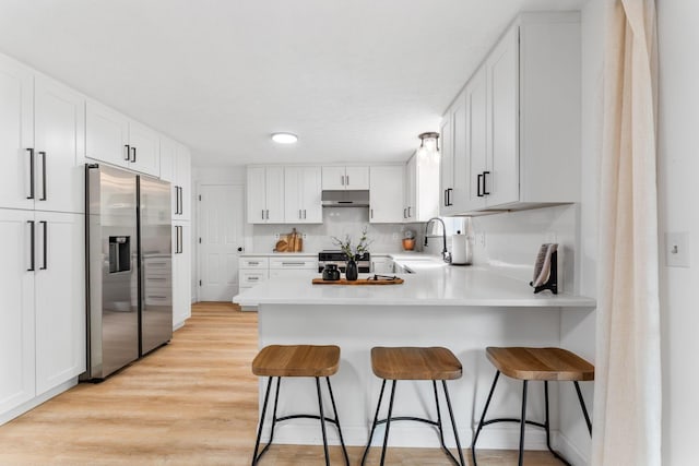 kitchen featuring a sink, a peninsula, under cabinet range hood, stainless steel appliances, and light wood-style flooring