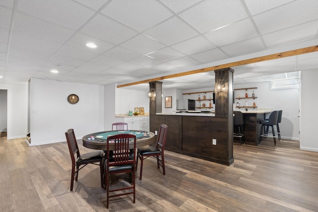 dining space with baseboards, wet bar, a drop ceiling, and wood finished floors