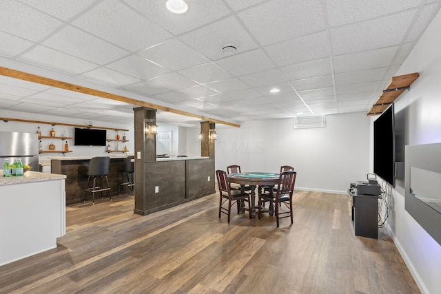 dining area featuring a drop ceiling, dark wood-style flooring, baseboards, and bar area