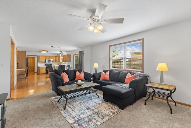 living area featuring light colored carpet, a textured ceiling, baseboards, and ceiling fan