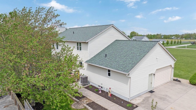 view of side of home with a shingled roof, a yard, and central AC