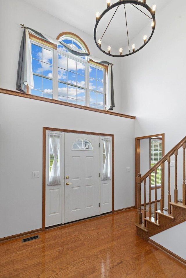 foyer with wood finished floors, visible vents, stairway, a high ceiling, and a notable chandelier