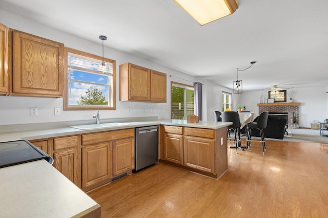 kitchen featuring a sink, a peninsula, pendant lighting, stainless steel dishwasher, and light wood-style floors