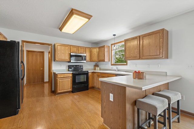 kitchen with a sink, a peninsula, black appliances, light wood finished floors, and a kitchen bar