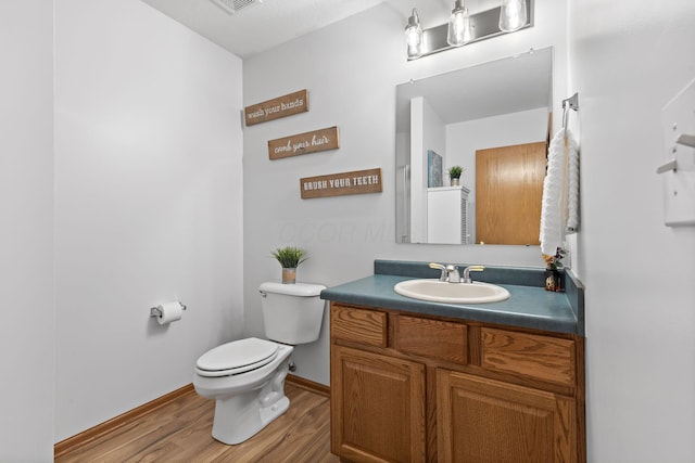 half bathroom featuring toilet, baseboards, wood finished floors, and vanity