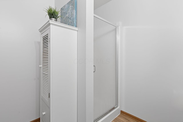 bathroom featuring baseboards, a shower stall, and wood finished floors