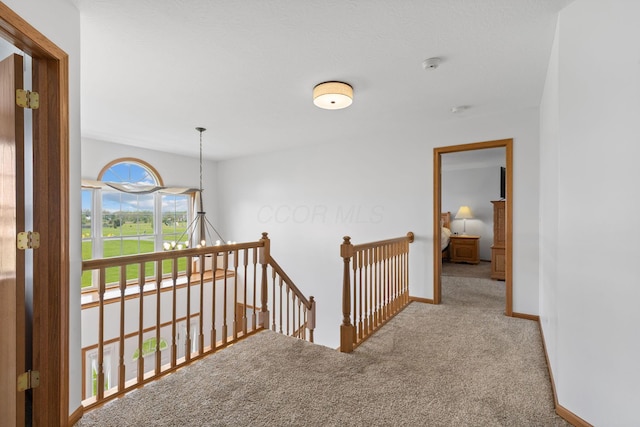 hall featuring an upstairs landing, baseboards, and carpet floors
