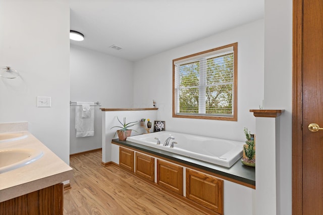 full bath with double vanity, wood finished floors, a sink, a bath, and visible vents