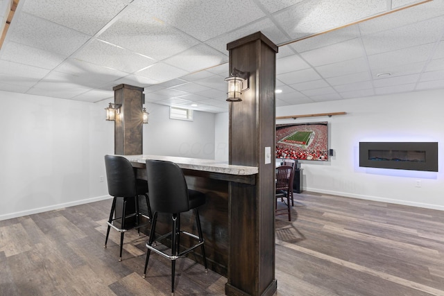 bar featuring a bar, a drop ceiling, baseboards, and dark wood-style floors