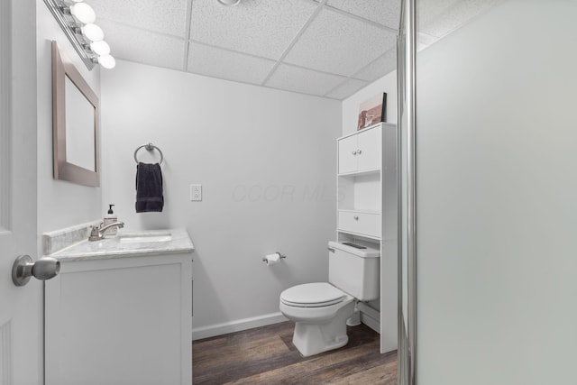 bathroom featuring baseboards, toilet, vanity, wood finished floors, and a paneled ceiling