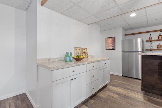 kitchen with freestanding refrigerator, a drop ceiling, dark wood finished floors, light countertops, and white cabinets