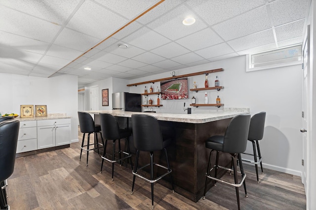 bar with a paneled ceiling, freestanding refrigerator, dark wood-style flooring, and wet bar