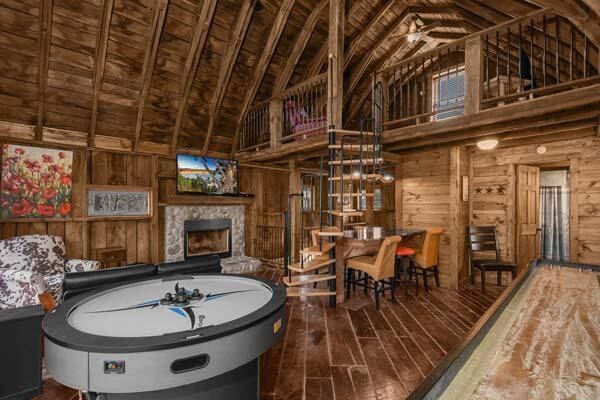 recreation room featuring a stone fireplace, wood walls, wood finished floors, and high vaulted ceiling