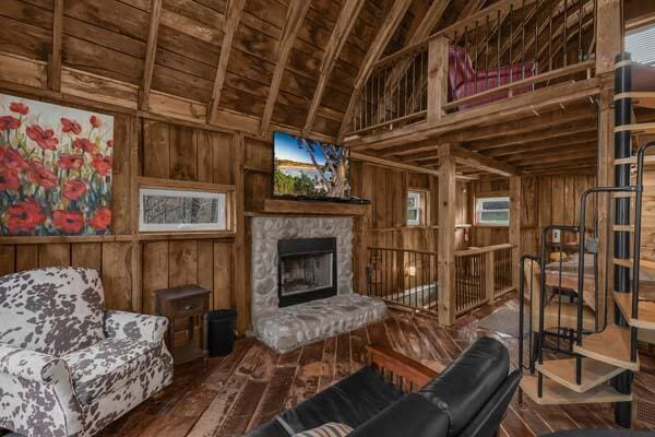 living room with hardwood / wood-style flooring, wood walls, and a stone fireplace