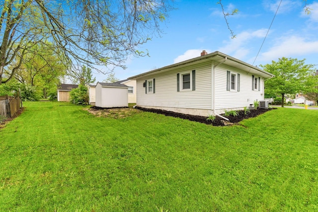 rear view of property with a storage unit, central AC, a chimney, and a yard