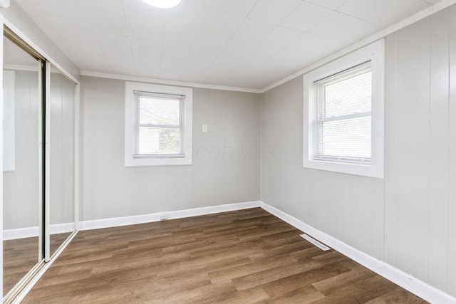 unfurnished bedroom featuring wood finished floors, a closet, crown molding, and baseboards