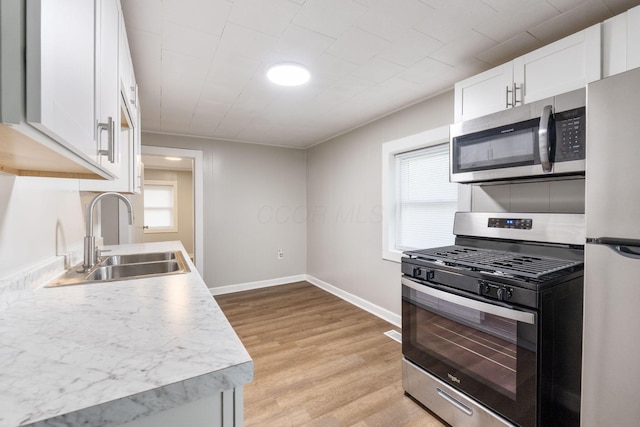 kitchen featuring stainless steel appliances, a sink, light wood-type flooring, white cabinetry, and light countertops