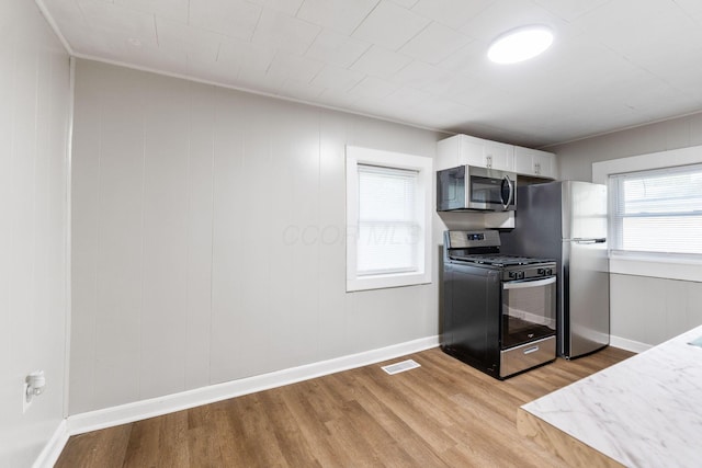 kitchen with stainless steel appliances, light wood-style flooring, white cabinets, and baseboards
