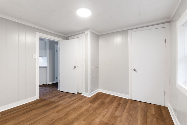unfurnished bedroom featuring wood finished floors, a decorative wall, ornamental molding, and baseboards