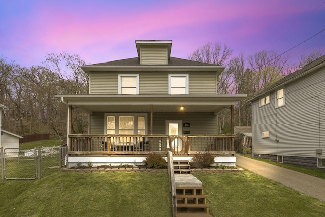 back of house at dusk with a porch, a yard, fence, and a gate