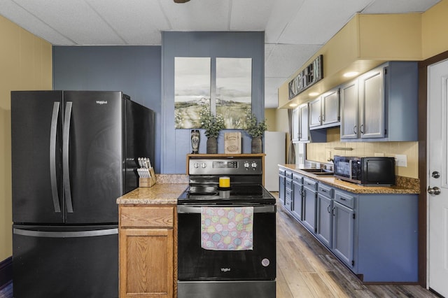 kitchen with black microwave, freestanding refrigerator, a drop ceiling, wood finished floors, and range with electric stovetop