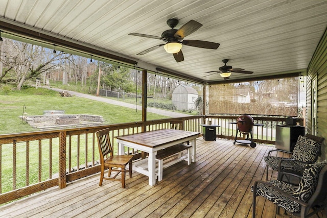 wooden terrace with outdoor dining area, ceiling fan, a yard, and an outdoor fire pit