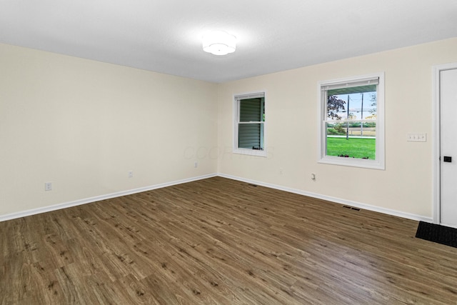 spare room with baseboards, dark wood-style flooring, and visible vents