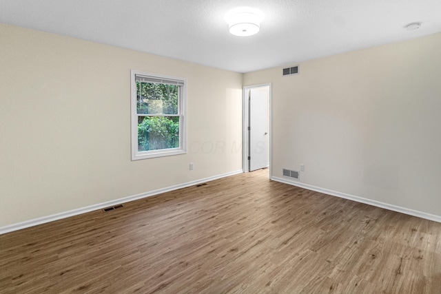 spare room with baseboards, wood finished floors, and visible vents
