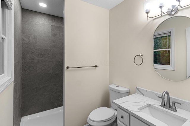 bathroom with toilet, a tile shower, and vanity