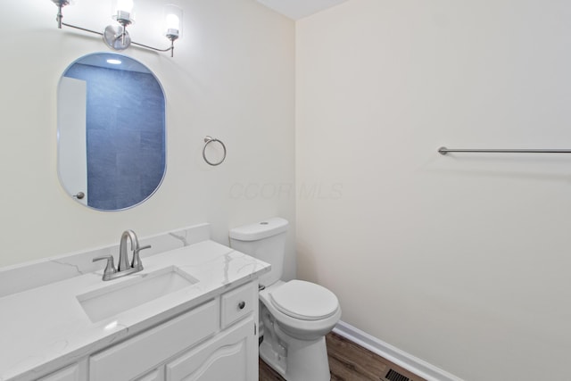 half bathroom featuring vanity, baseboards, toilet, and wood finished floors