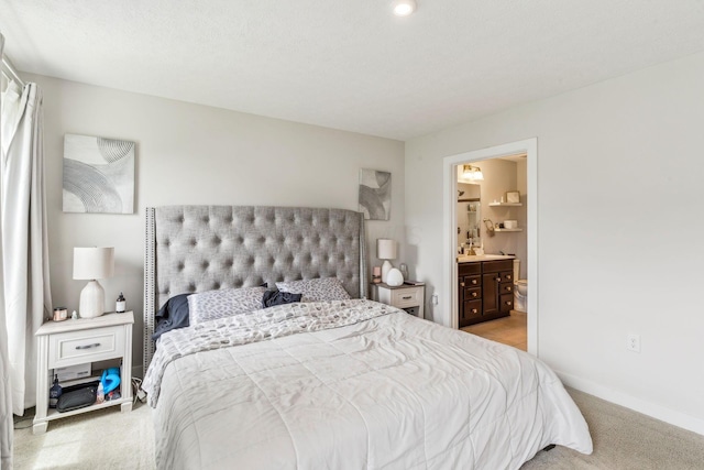 bedroom featuring light colored carpet, baseboards, and ensuite bath
