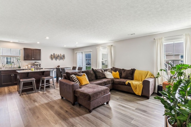 living area with recessed lighting, a textured ceiling, visible vents, and light wood finished floors