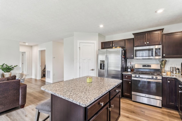 kitchen featuring light stone countertops, dark brown cabinets, open floor plan, a center island, and stainless steel appliances