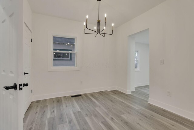 empty room featuring an inviting chandelier, baseboards, and light wood-type flooring