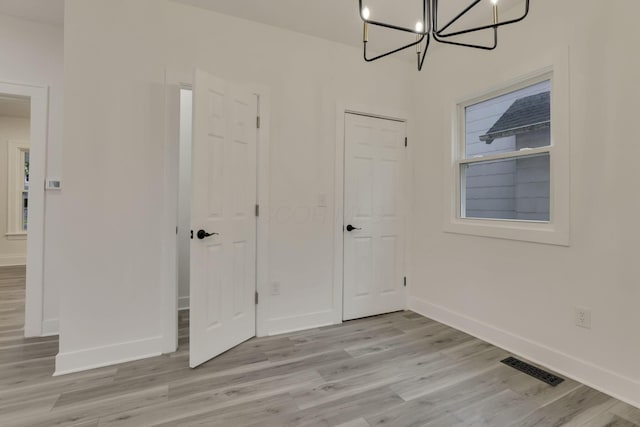 interior space featuring visible vents, light wood finished floors, baseboards, and a chandelier