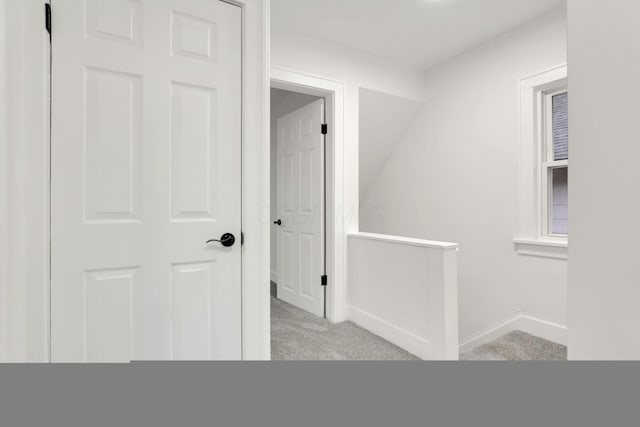 hallway featuring baseboards, carpet flooring, and an upstairs landing