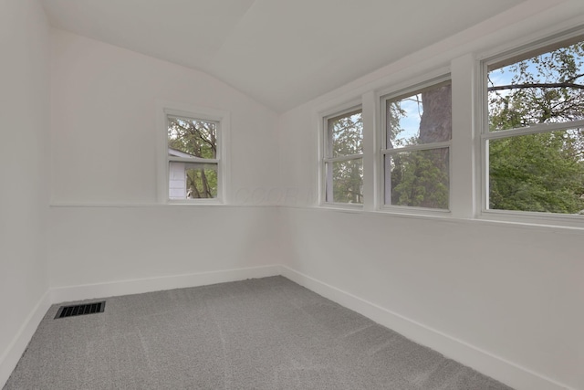 carpeted spare room featuring baseboards, vaulted ceiling, and visible vents