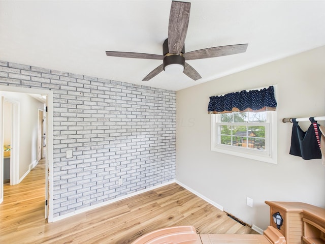 interior space featuring baseboards, a ceiling fan, light wood finished floors, and brick wall