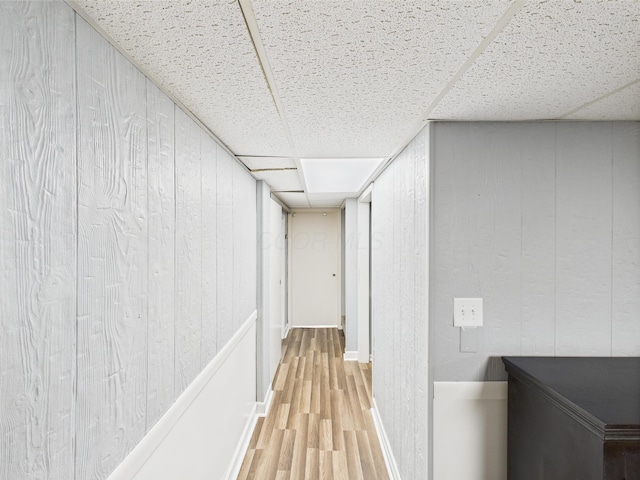 corridor featuring wooden walls, a drop ceiling, and wood finished floors