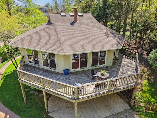 rear view of house with roof with shingles, a wooden deck, and a chimney