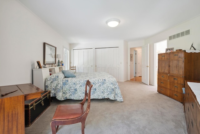 bedroom with multiple closets, light colored carpet, and visible vents